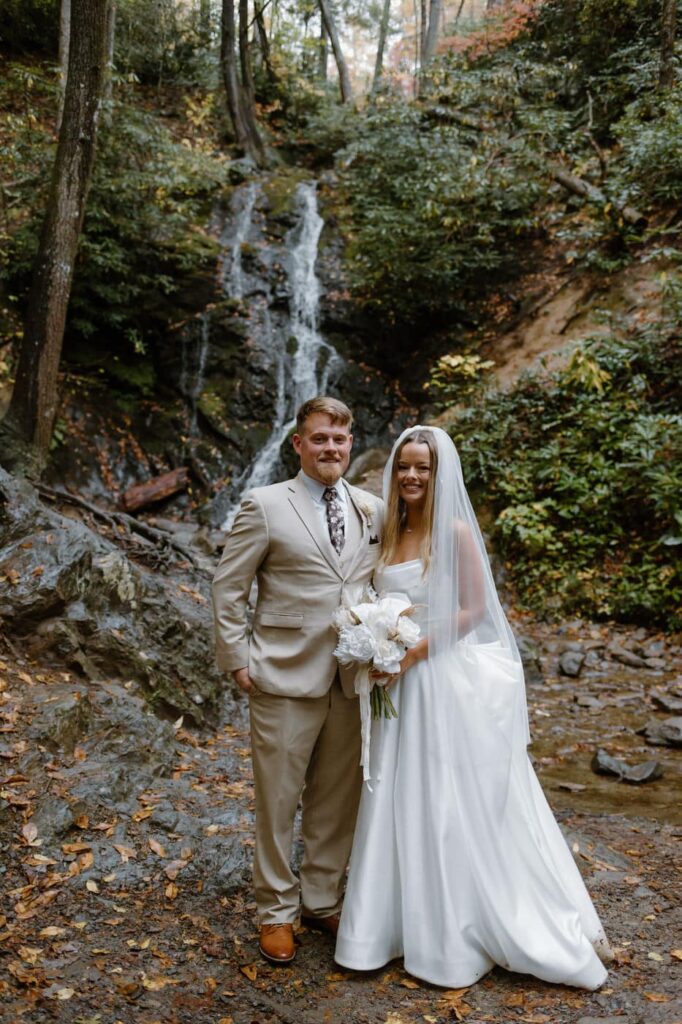 Bride and groom smile for their portraits in front of a small waterfall during their Great Smoky Mountain elopement.