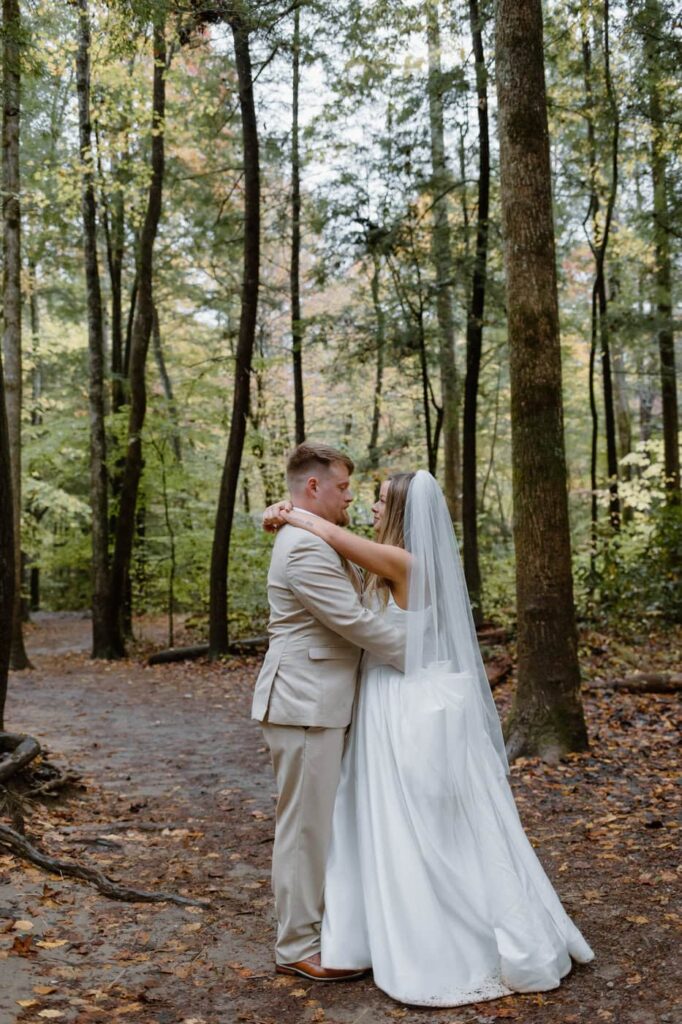 Couple stands surrounded by nature and tall trees while taking their bride and groom portraits during their Great Smoky Mountain elopement.