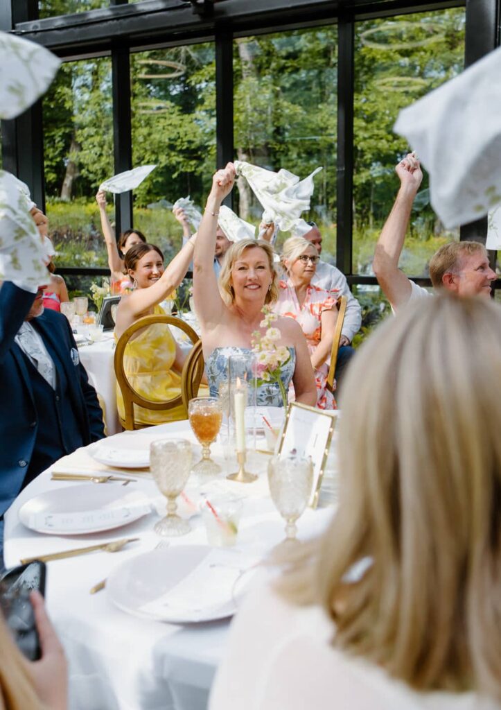 Fun reception photo of mother of the bride twirling napkin in the air to welcome in the bride and groom at Nichols Heir, Glass House.
