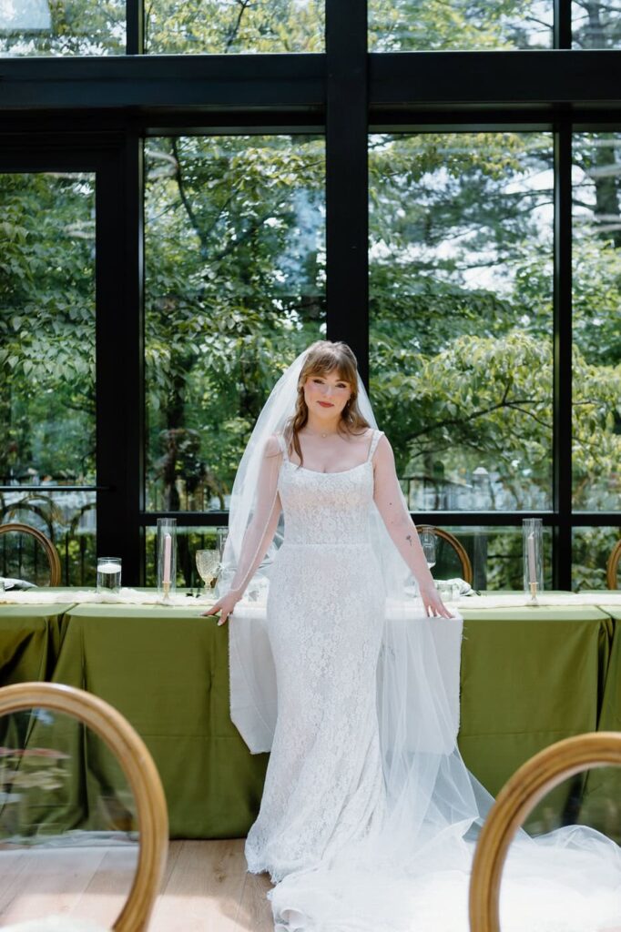 Bride poses in front of reception table at Nichols Heir wedding venue, The Glass House.
