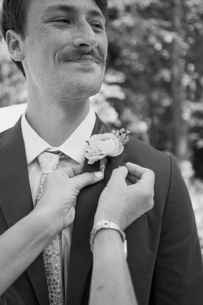 Mother of the groom helps pin the groom's boutonniere to his suit jacket.