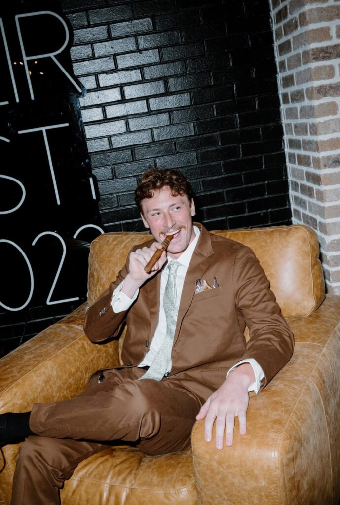 Groom in brown suit smokes cigar before walking down the aisle at modern wedding venue in Tennessee.
