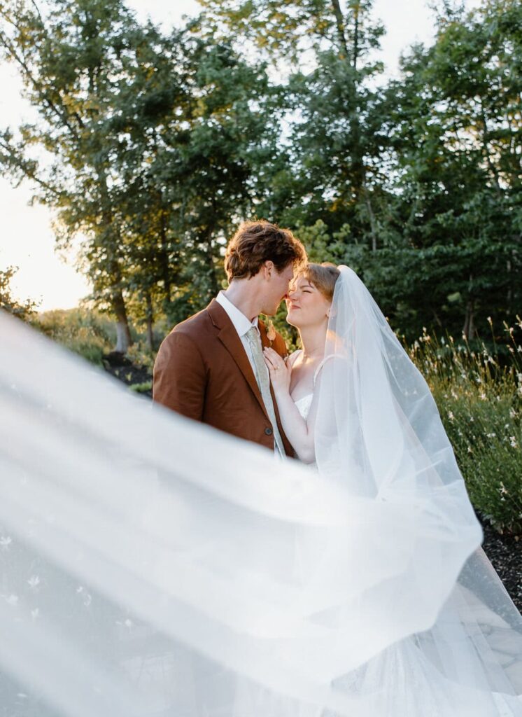 Beautiful golden hour portrait of bride and groom with a cathedral veil layered over the couple.