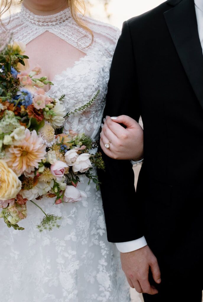 Lace overlay wedding dress paired with fall floral bouquet. While the groom is in black tie wedding attire at Ancient Lore Village, Knoxville wedding venue.