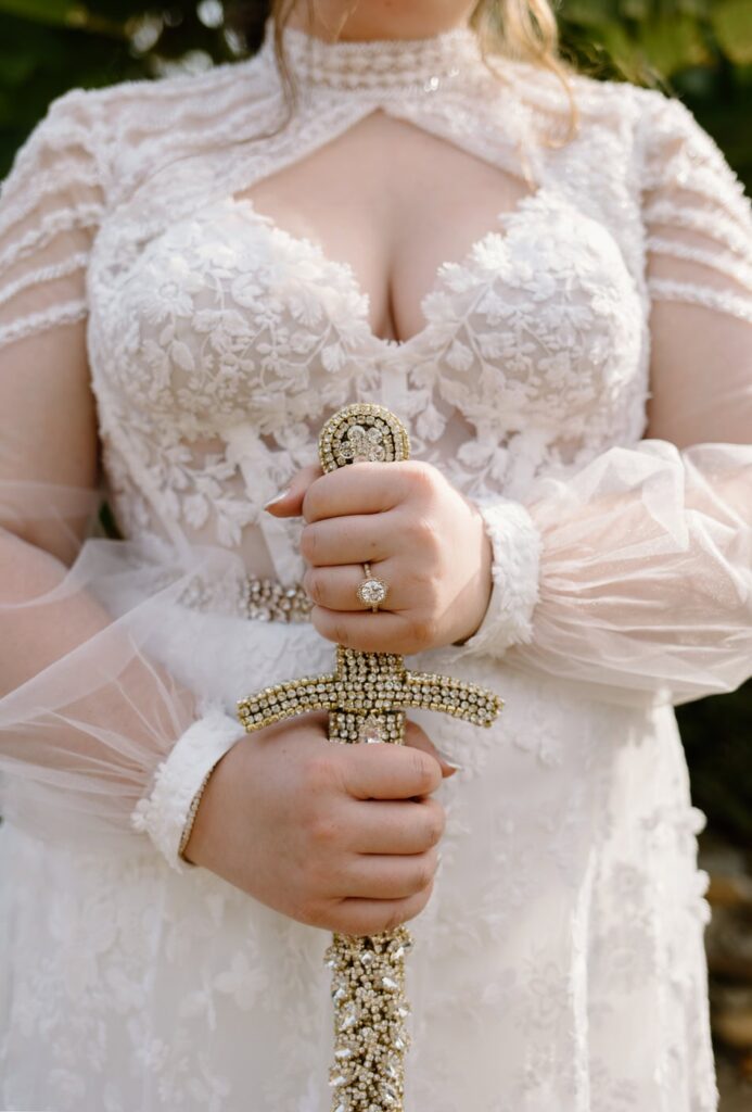 Bride holds a custom jeweled sword gifted to her on her wedding day. The perfect fairytale gift for a wedding at Ancient Lore Village, a Knoxville wedding venue.