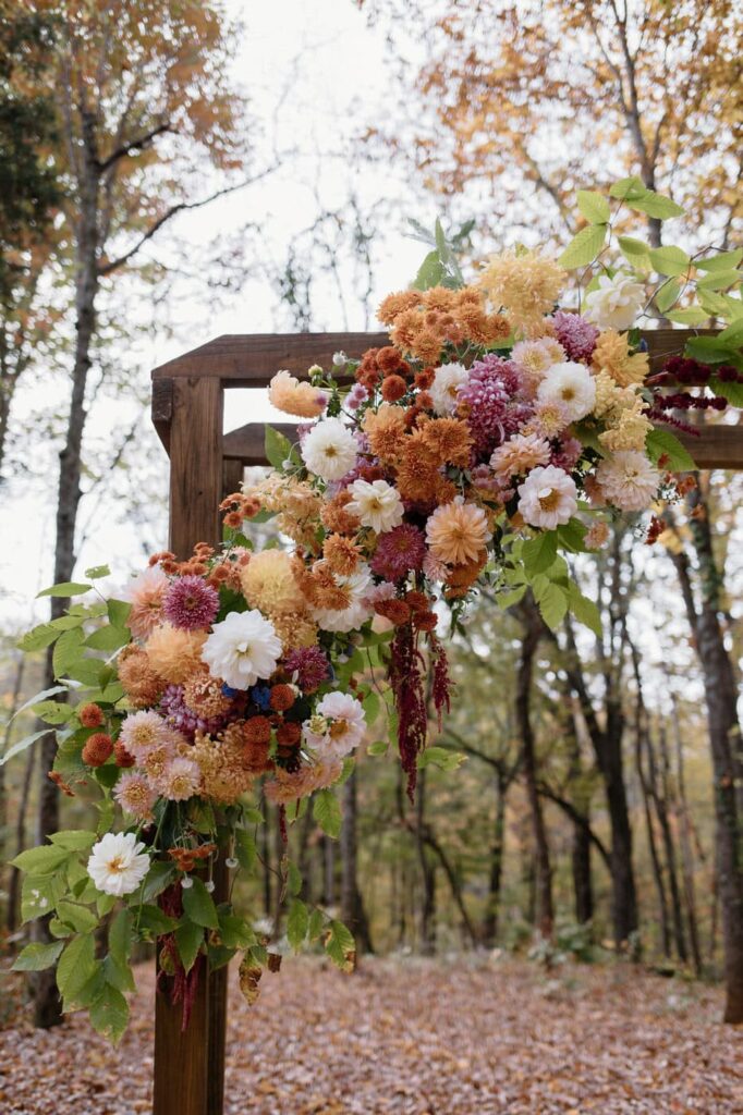Fall wedding arbor with muted oranges, yellows, and pinks at the wooded ceremony space at Ancient Lore Village, Knoxville Wedding venue.
