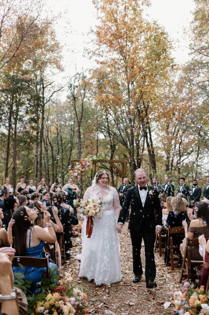 Bride and groom recess down the aisle with bubbles at fall wedding ceremony at Ancient Lore Village, Knoxville wedding venue.